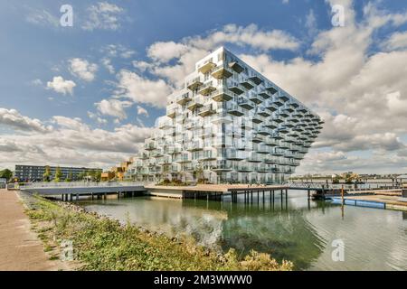 un complesso di appartamenti sul bordo dell'acqua con barche ancorate in fronte - bruciature e altri edifici Foto Stock