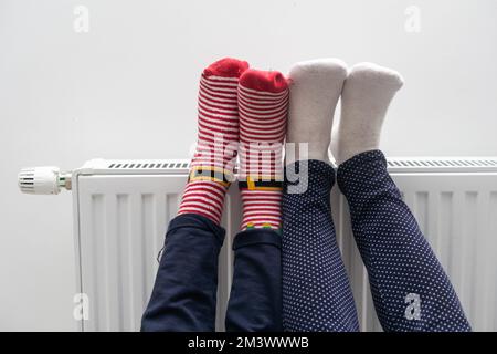 Madre e bambino che scalda i piedi vicino al riscaldatore a casa, primo piano Foto Stock