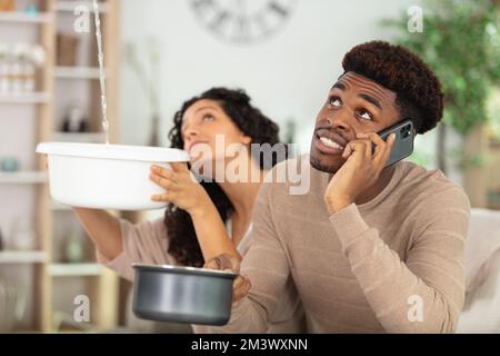 giovane coppia che raccoglie l'acqua nel secchio dal soffitto in casa Foto Stock