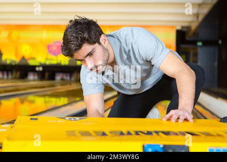 uomo che raccoglie la palla da bowling dal rack nel club Foto Stock