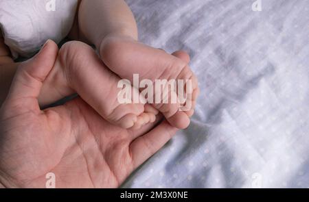 Le mani femminili tengono le gambe del bambino su uno sfondo grigio da vicino. Foto di alta qualità Foto Stock