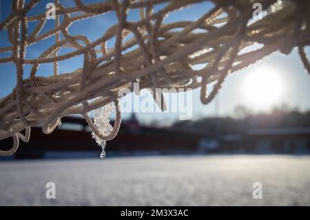 primo piano di ghiaccio sciolto sulla rete di gol sul campo da calcio coperto di neve. Foto Stock