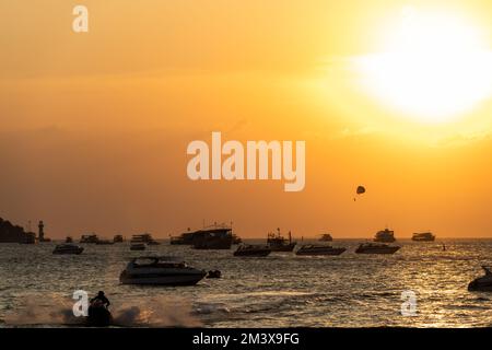 Qualcuno parasaila sopra le barche dei turisti e moto d'acqua durante il tramonto a Pattaya Beach. Vita quotidiana a Pattaya, provincia di Chonburi, Thailandia il 17 dicembre 2022. L'area, ben nota ai turisti, è una delle aree chiave che l'autorità del Turismo della Thailandia (TAT) ha promosso per attrarre più turisti stranieri nel paese, uno sforzo per salvare la sua economia dipendente dal turismo. Foto Stock