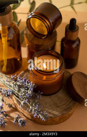 Candele di soia in un vaso di vetro. Aromaterapia. Candela e lavanda brucianti. Coperchio in legno per vasetti. Sfondo beige. Comfort e relax. Fatto a mano. Decorazioni per la casa. Foto Stock