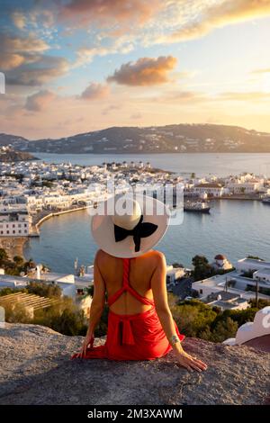 Un'elegante donna turistica in un vestito rosso gode della vista sulla città di Mykonos Foto Stock
