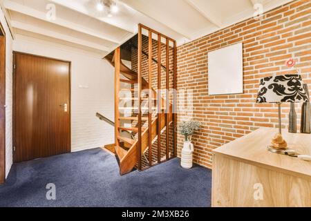 camera con pareti in mattoni e moquette blu, dotata di una scala in legno che conduce al secondo piano in un appartamento Foto Stock