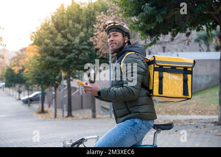 Concetto di consegna degli alimenti. Giovane pilota nero con smartphone in città dall'aspetto zaino Foto Stock