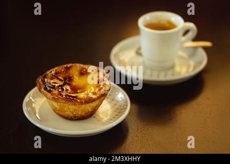 Colazione estiva portoghese. Pastello de nata e piccolo caffè. Crostata dolce all'uovo su tavola nera. Foto Stock