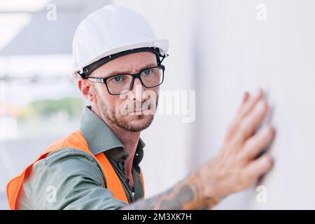 costruttore lavoratore guardare a costruzione intonacando muro per dettagli di alta precisione e qualità per una buona costruzione a casa Foto Stock