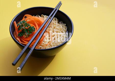 tagliatelle di ramen vegetariane con bacchette su sfondo giallo Foto Stock