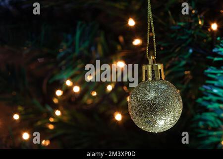 Goiânia, Goias, Brasile – 17 dicembre 2022: Una palla d'oro, appesa al ramo con dettagli dell'albero di Natale e luci sullo sfondo. Foto Stock