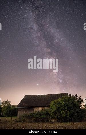 Uno scatto verticale della Via Lattea e del cielo stellato su una piccola casa rurale Foto Stock