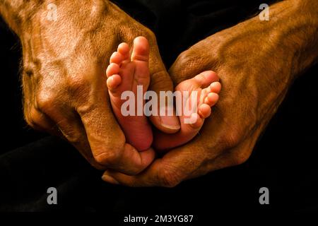 I piedi piccoli di una bambina sono messi tra le mani di suo padre Foto Stock