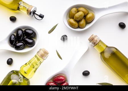 Cucchiai di olive gialle gialle nere con bottiglie d'olio Foto Stock