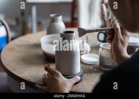 Donna professionista proprietario piccola impresa ceramica tiene pennello in mani e processi in miniatura vaso Foto Stock