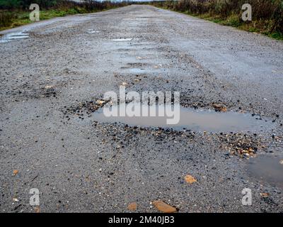 Pothole su una strada asfaltata in una giornata invernale piovosa. Concetto di rischio e problemi di traffico Foto Stock