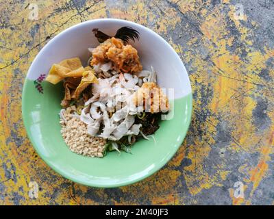 Spaghetti all'uovo giallo secco con gamberi, pollo a fette e wonton in una ciotola su fondo di cemento. Cibo di strada asiatico, Thailandia. Foto Stock