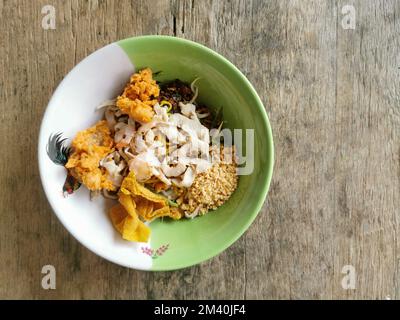 Spaghetti all'uovo giallo secco con gamberi, pollo a fette e wonton in una ciotola su sfondo tavolo di legno. Cibo di strada asiatico, Thailandia. Foto Stock