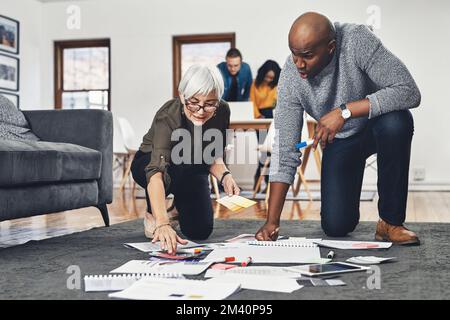 Questa configurazione è semplice ma efficace. Foto a tutta lunghezza di due uomini d'affari che guardano i documenti mentre lavorano sul pavimento del loro ufficio. Foto Stock