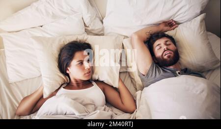 Oggi andremo in una clinica del sonno. una giovane donna che copriva le orecchie con un cuscino mentre il marito russava a letto. Foto Stock
