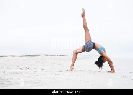 La combinazione perfetta di forza, equilibrio e bellezza. una giovane donna che fa un cavalletto in spiaggia. Foto Stock