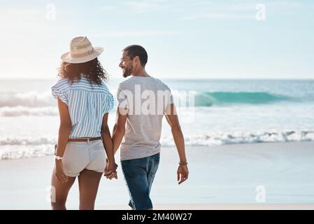 Al mio fianco, la vita al meglio con te. Ripresa da dietro di una giovane coppia che cammina lungo la spiaggia. Foto Stock