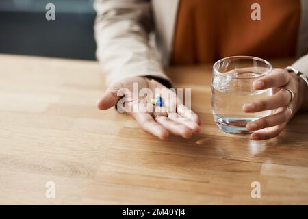 Ho davvero bisogno di queste pillole. una donna d'affari irriconoscibile che prende le pillole con un bicchiere d'acqua mentre nel suo ufficio. Foto Stock