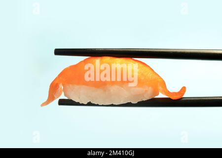 Cucina tradizionale giapponese. Delizioso sushi nigiri con sakè di salmone su sfondo blu. sushi sulle bacchette in primo piano. Foto Stock