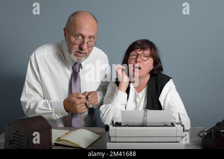 Sul luogo di lavoro. L'anziano Boss e il suo esperto segretario in ufficio. Stile retrò. Vecchia macchina da scrivere e telefono sul tavolo. Foto Stock