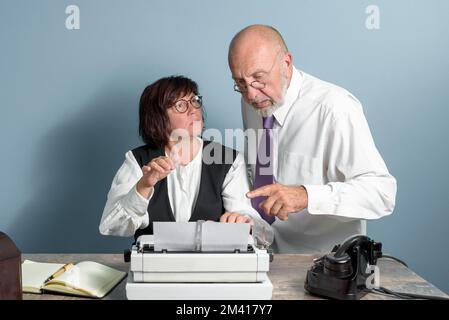 In ufficio. Stile retrò. Capo anziano che dettava il testo al suo segretario. Donna lavora sulla vecchia macchina da scrivere manuale. Foto Stock
