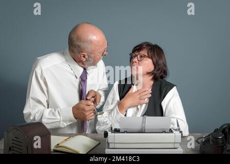 Il tempo è trascorso! Ambiente di lavoro retrò. Capo anziano che parla con la sua segretaria espiata donna puntando il dito a guardare. Macchina da scrivere manuale sul tavolo. Foto Stock