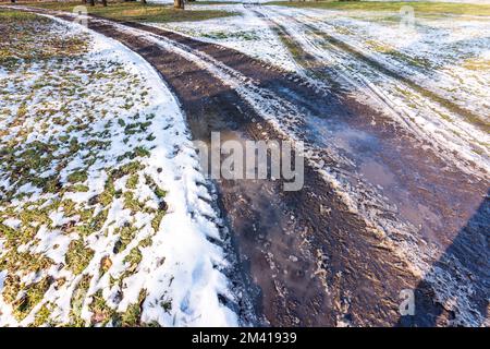 Piccola pozza sulla strada, riflesso in acqua vicino al prato. Neve e inverno Foto Stock