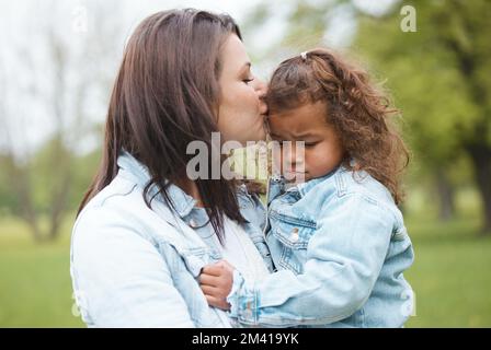 Amore, parco e madre baciano il bambino con l'espressione sconvolta, triste e infelice sul viso per lasciare il parco giochi. Famiglia, sostegno e mamma baciare la giovane ragazza per Foto Stock