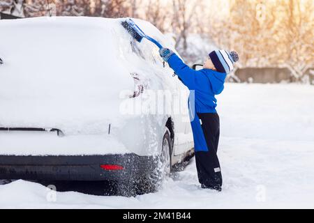 bambino che aiuta a spazzolare la neve dalla macchina dei genitori Foto Stock