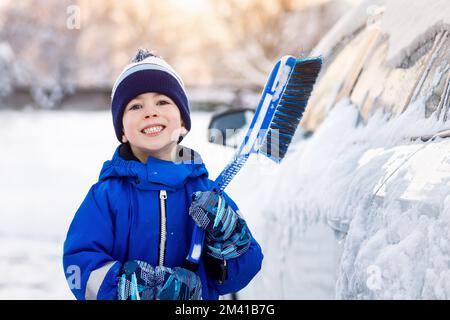 ragazzino con spazzola per pulire la neve dall'auto Foto Stock