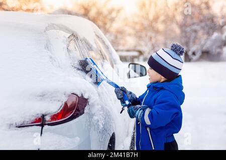 bambino che aiuta a spazzolare la neve dalla macchina dei padri Foto Stock