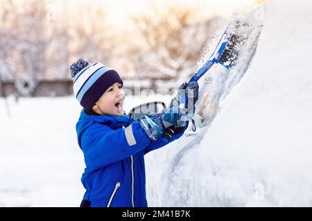 bambino piccolo che aiuta a pulire la neve dalla macchina dei genitori Foto Stock