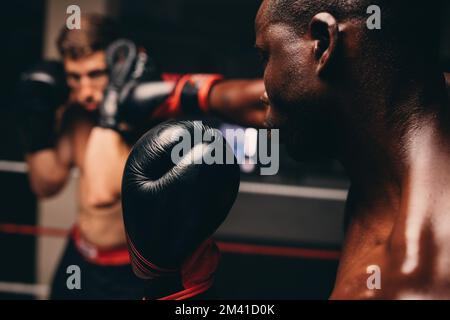 Boxer colpisce il suo partner sparring con un pugno in un anello di pugilato. Due giovani pugili si allenano insieme in una palestra di pugilato. Foto Stock