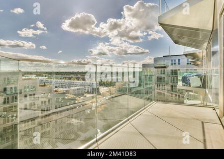 un'area esterna con edifici e nuvole nel cielo come si vede da una ringhiera di vetro su un balcone che si affaccia su una città Foto Stock