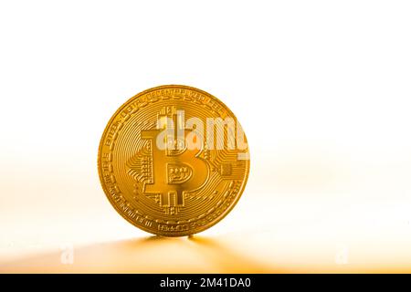 Moneta bitcoin oro posta su sfondo bianco alla luce del tramonto. Simbolo valuta virtuale. Foto Stock