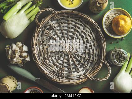 Cibo sano sfondo con vassoio vuoto cerchio di vimini e ingredienti di cottura: Finocchio, limone, olio e condimento sul tavolo verde, vista dall'alto Foto Stock