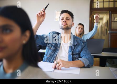 Gli studenti fanno domande, sollevano le mani e si apprendiano in aula per l'apprendimento, l'istruzione o il college con un notebook sulla scrivania. Gruppo di studenti universitari, classe universitaria o. Foto Stock