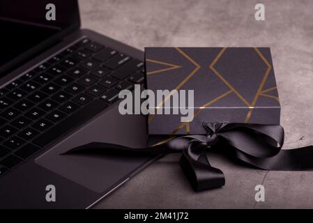 Confezione regalo nera decorata con strisce dorate su una tastiera per computer portatile. Regali per gli uomini. Buon per i Banners in linea di acquisto del giorno del padre o del venerdì nero. Foto Stock