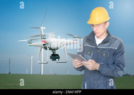 Ingegnere con computer tablet controlla drone su uno sfondo di turbine eoliche Foto Stock