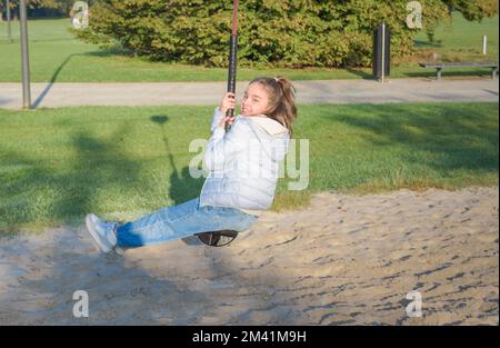 Giovane ragazza in sella a un bungee appeso. Divertimento autunnale all'aperto. nel parco giochi Foto Stock