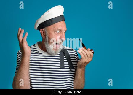 WOW. Vecchio ritratto marinaio sorpresa e ammirazione. Tubo fumante, forma marina. su uno sfondo blu isolato Foto Stock