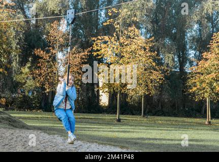 Giovane ragazza in sella a un bungee appeso sul parco giochi. Divertimento autunnale all'aperto. Foto Stock