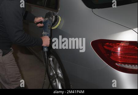 Inizio della lucidatura dell'automobile. Addetto al servizio auto con lucidatore elettrico lucidante cappa d'argento in officina di riparazione auto Foto Stock