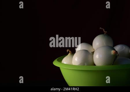 Cipolle pelate in un colino di plastica verde su fondo nero. Spazio di copia Foto Stock