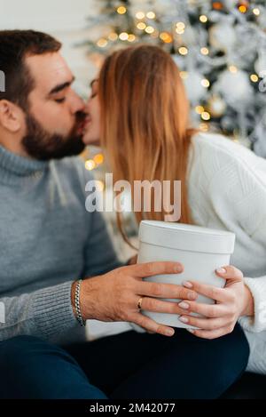 coppia felice vicino a scatole regalo e albero di natale. coppia abbracciandosi e guardandosi vicino all'albero di natale. Foto Stock